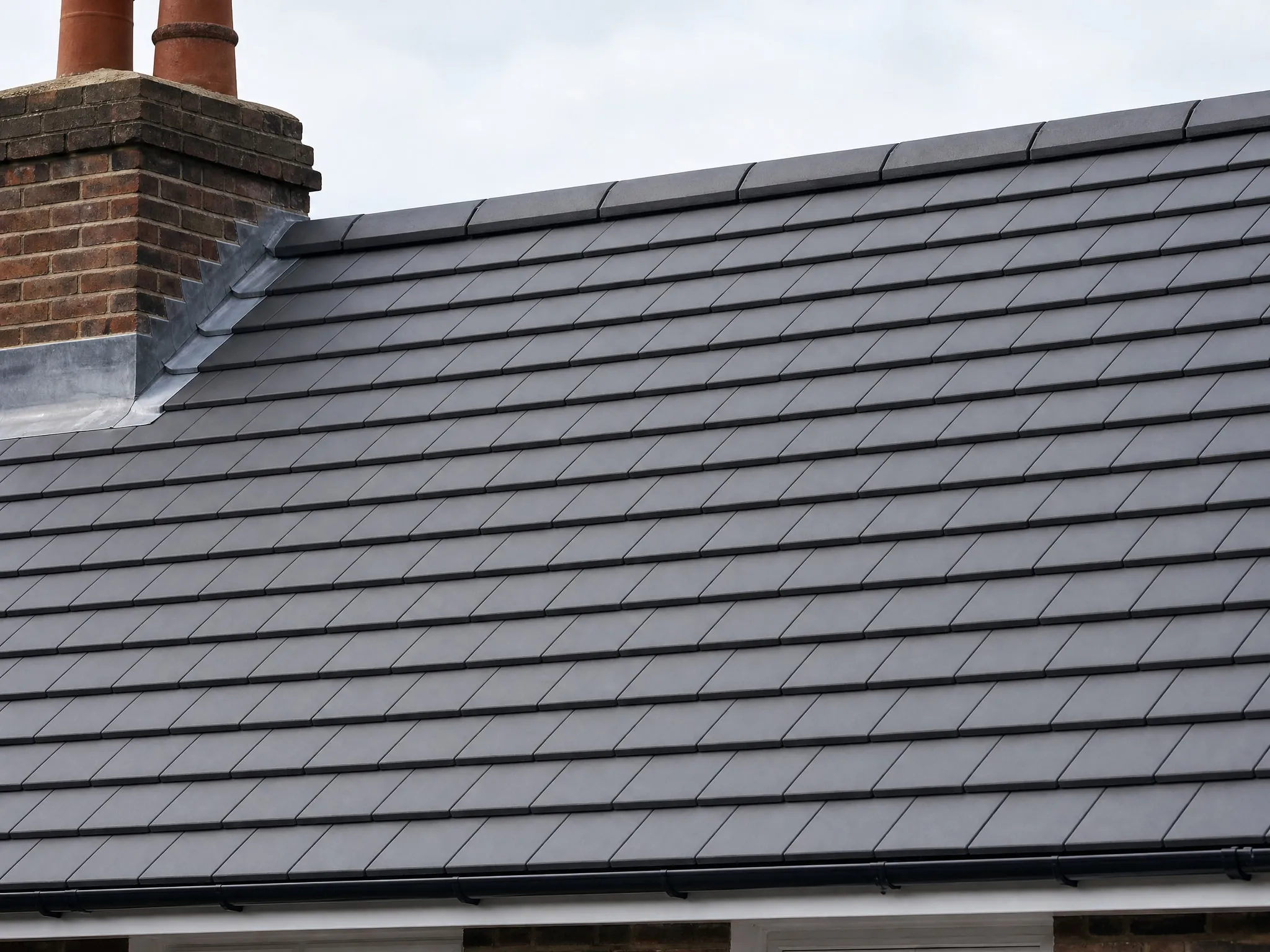 Newly tiled pitched roof in dark grey tiles with a dry ridge and lead flashing at the chimney