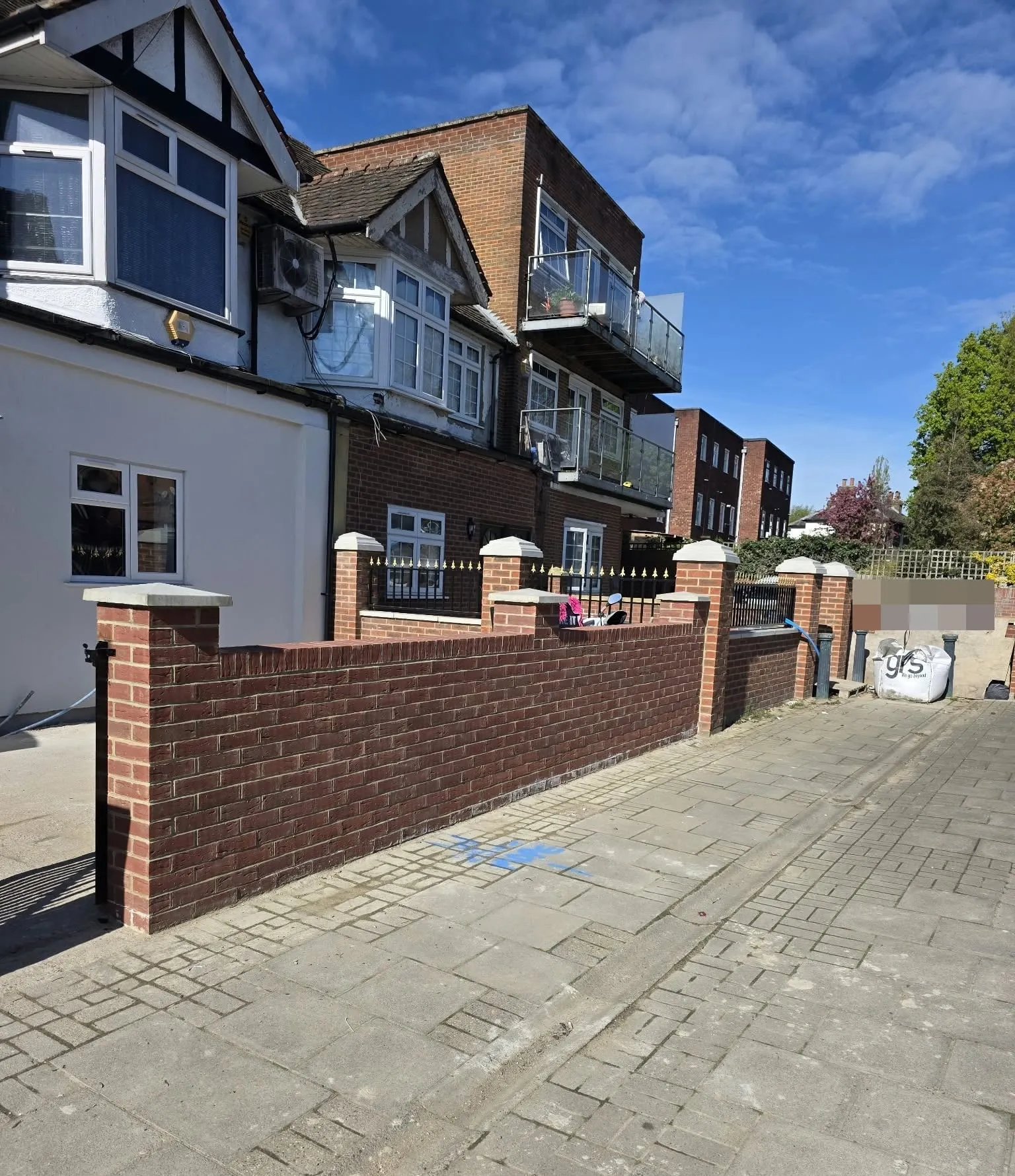 New red brick front wall with stone-capped pillars and railings, behind a paved pavement
